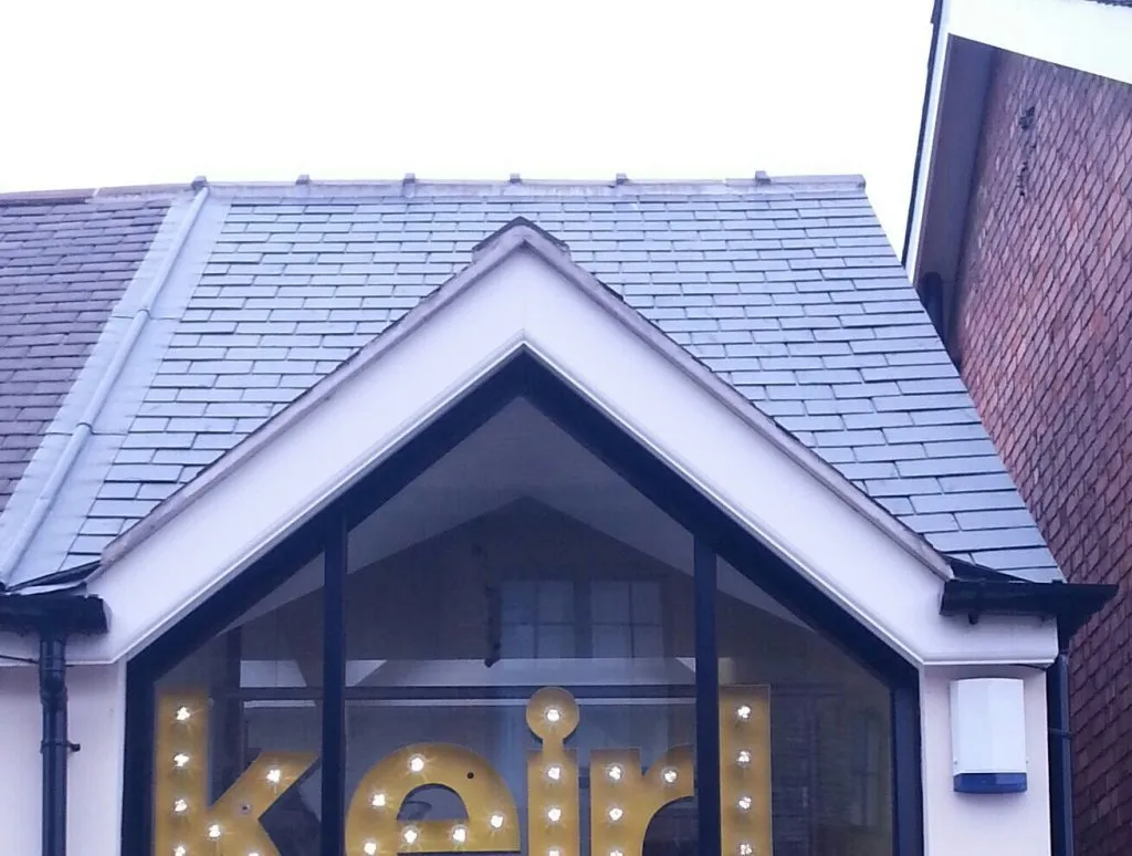 Modern pitched roof with grey slate tiles and a prominent windowed dormer/gable on a building.