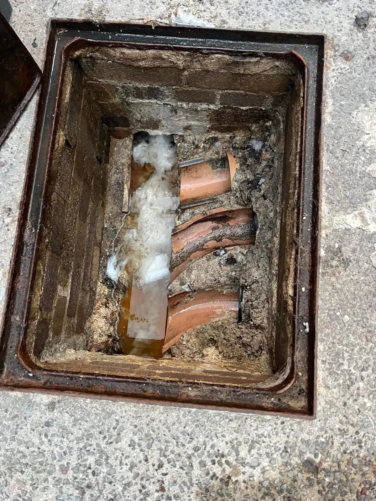 Severe blockage in a drain manhole with broken pipes and debris