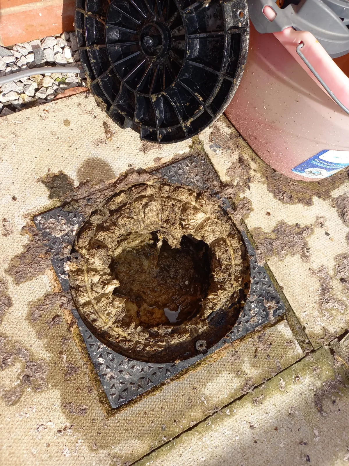 Close-up of an extremely blocked outdoor drain or gully, overflowing with a dense build-up of grease and waste.