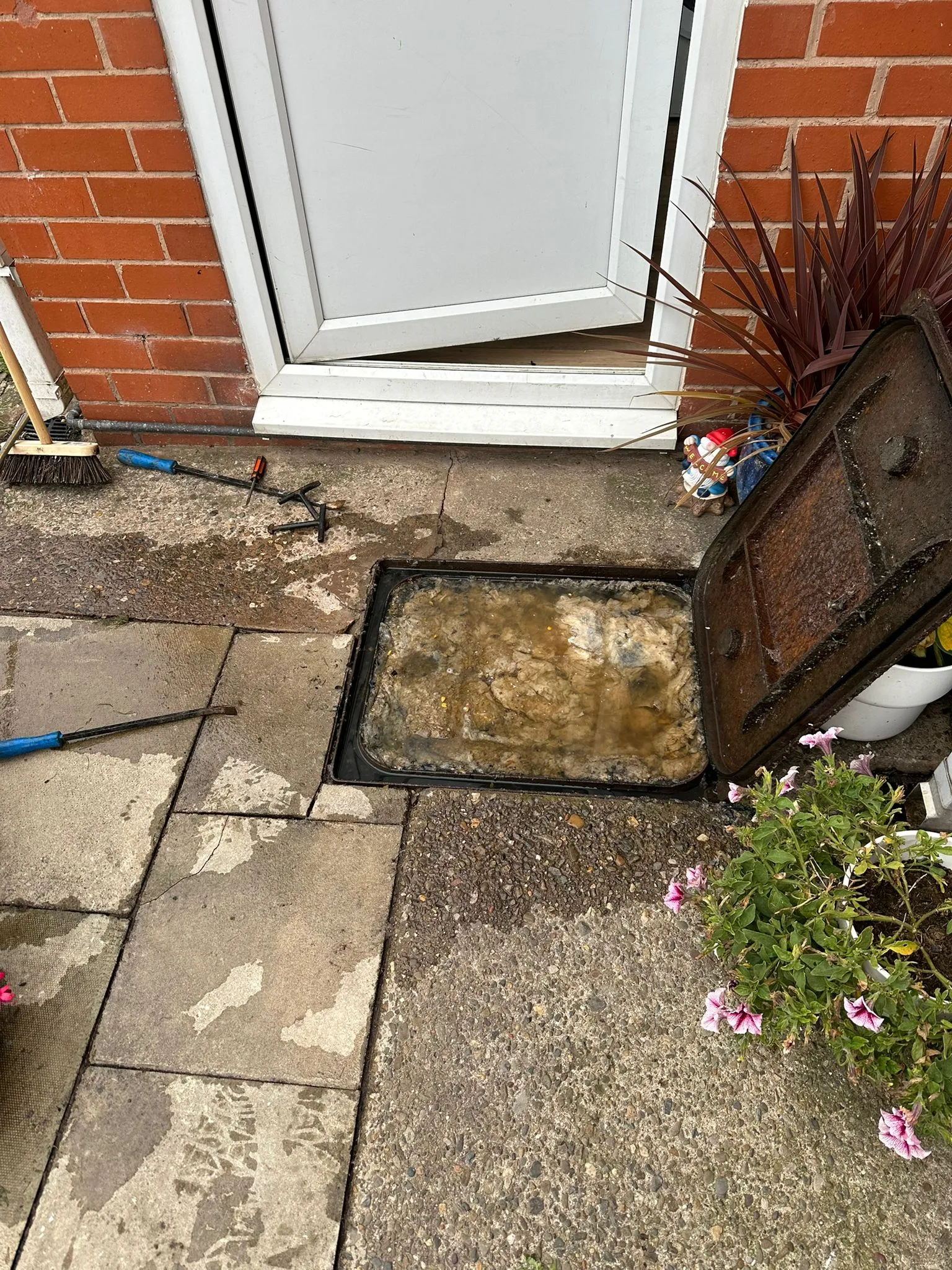 A severely blocked external domestic drain or manhole overflowing with wastewater and debris on a paved patio.