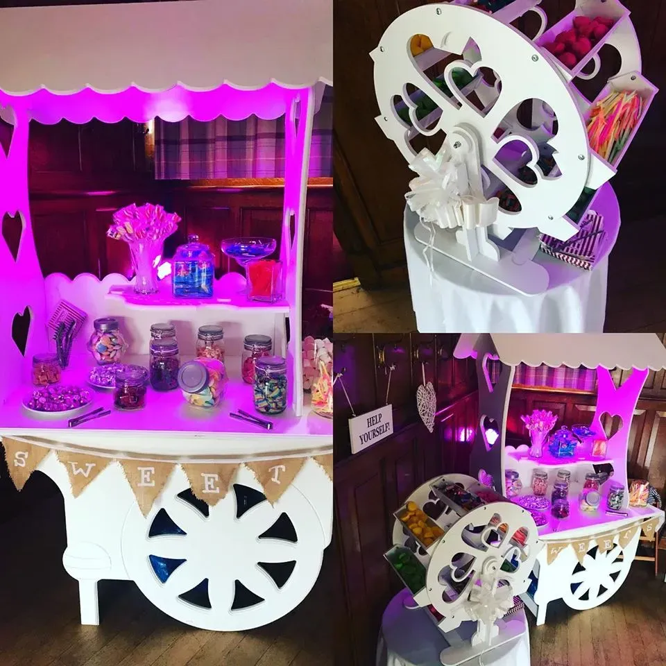 A white candy cart and sweet Ferris wheel filled with colourful sweets and illuminated by pink lights.