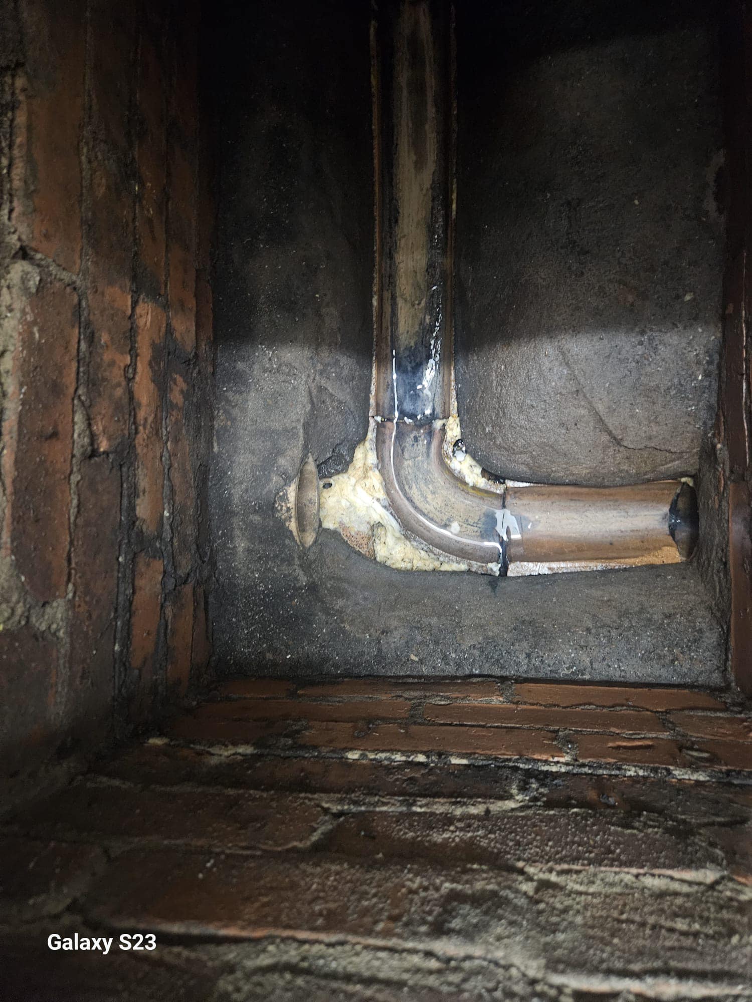 Old, corroded drainage pipes set against a brick wall, indicating wear and potential damage.