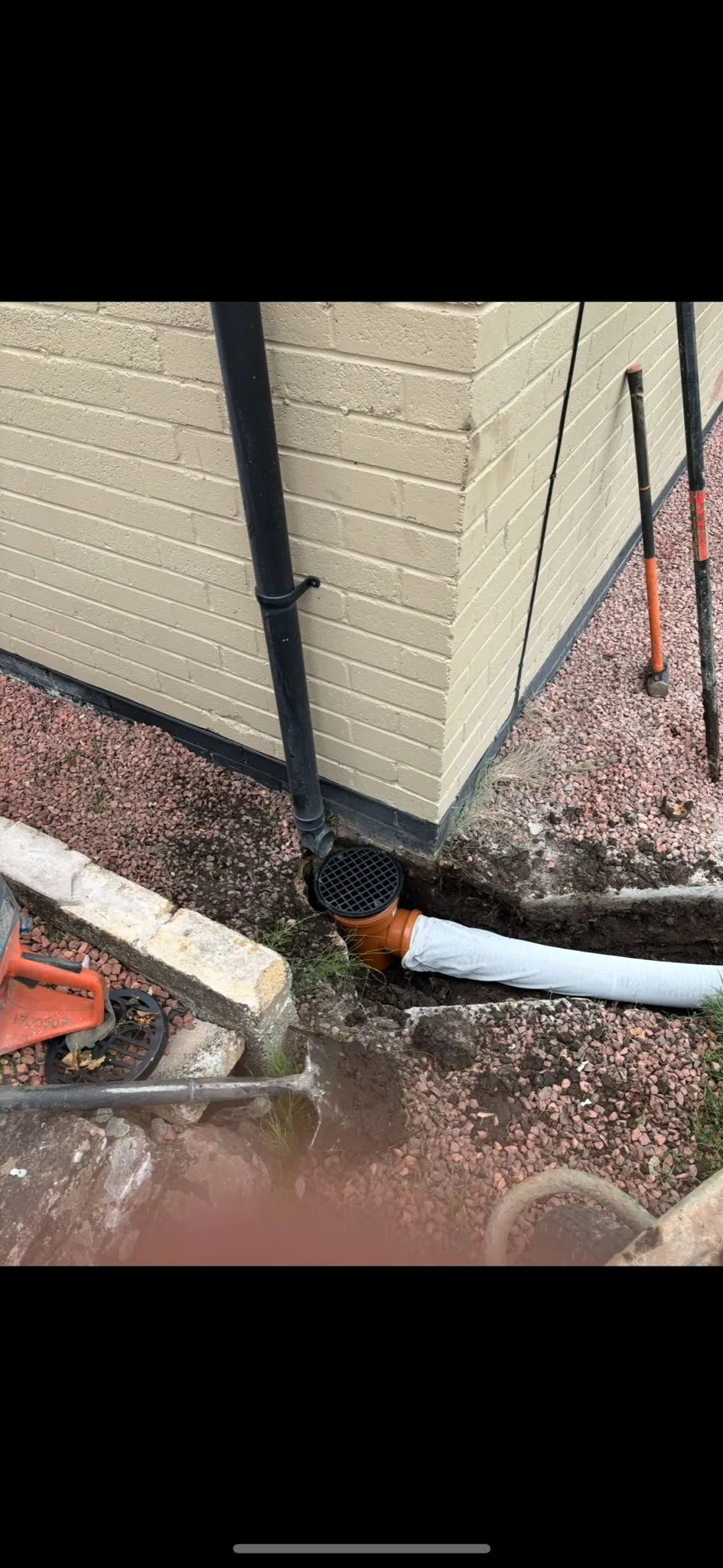 Drainage excavation for pipe installation at a building's foundation.
