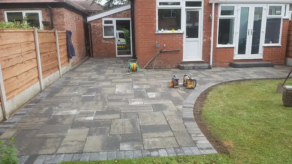 Newly laid grey and charcoal block paving patio or paved area next to a green lawn.