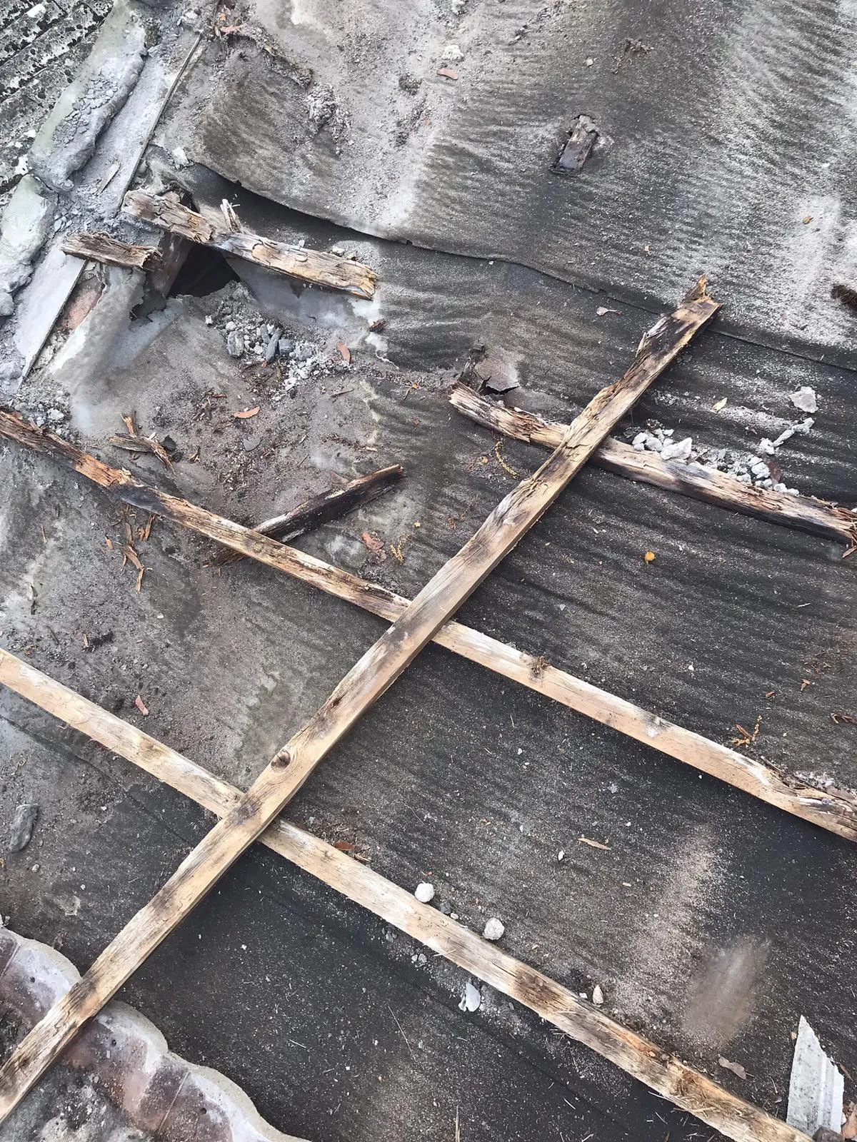 Damaged flat roof with exposed wooden battens and underlayment during repair or renovation.