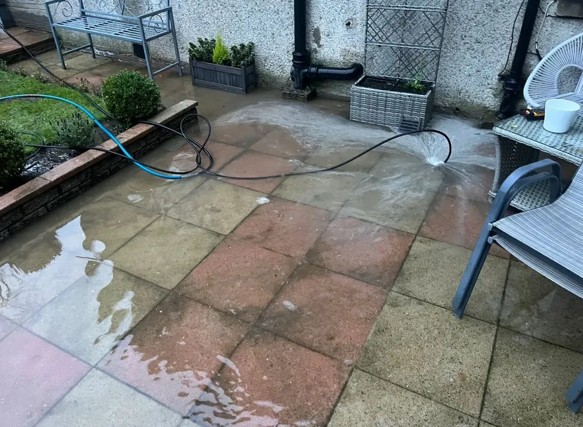 High-pressure water jet clearing a blocked outside drain causing flooding on a patio