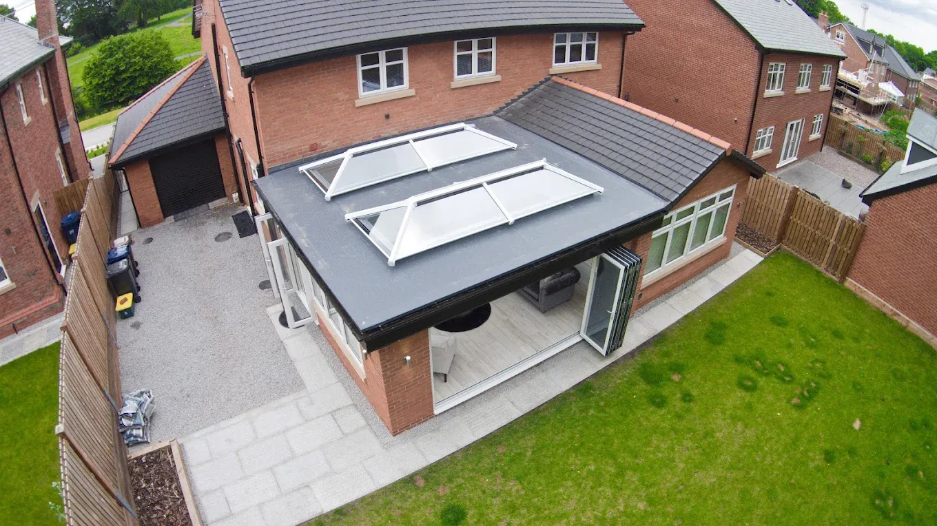 Modern house extension with flat roof, two roof lanterns, and bi-fold doors opening onto a patio.