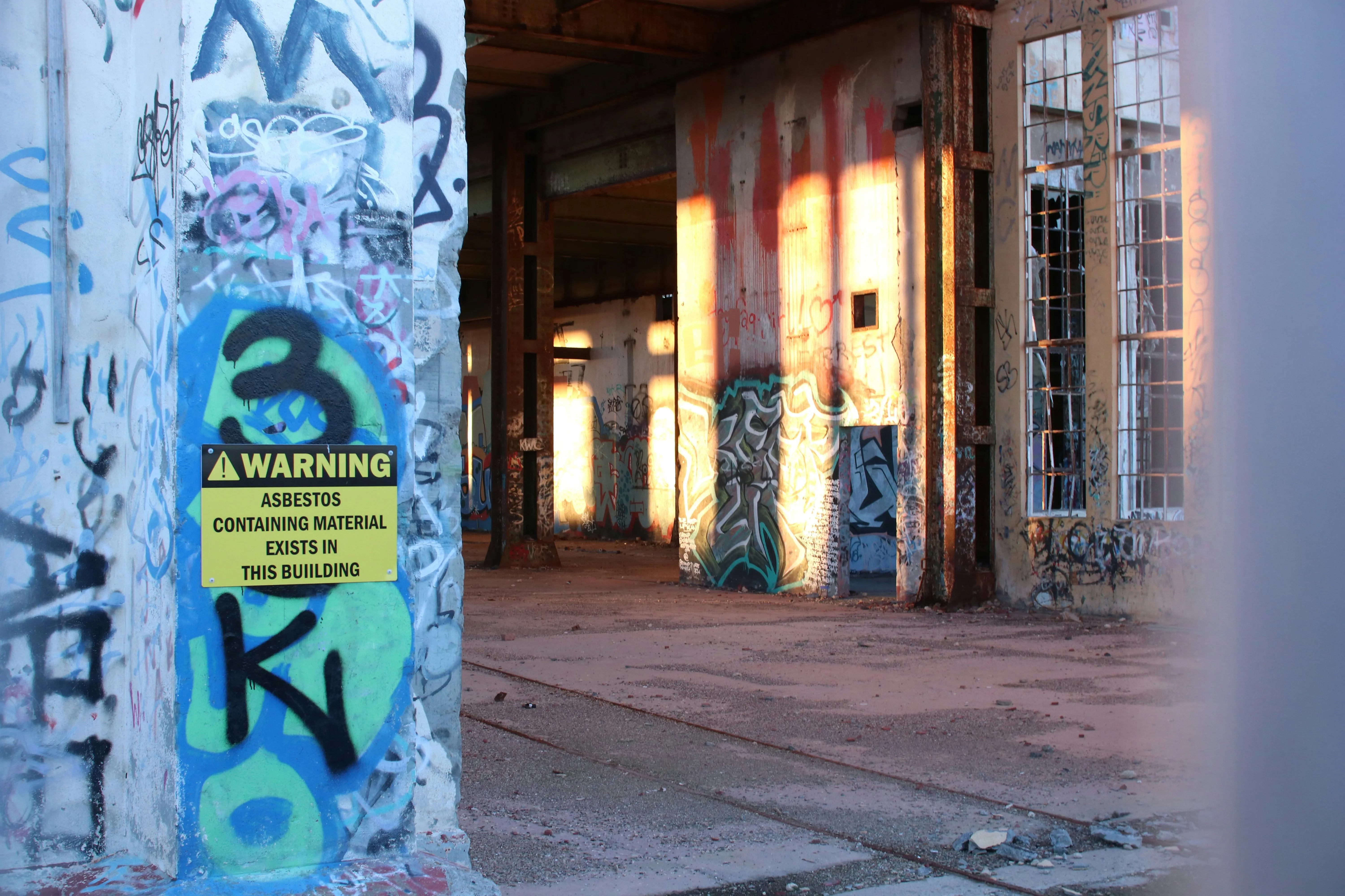 Interior of an abandoned building with graffiti and an asbestos warning sign.