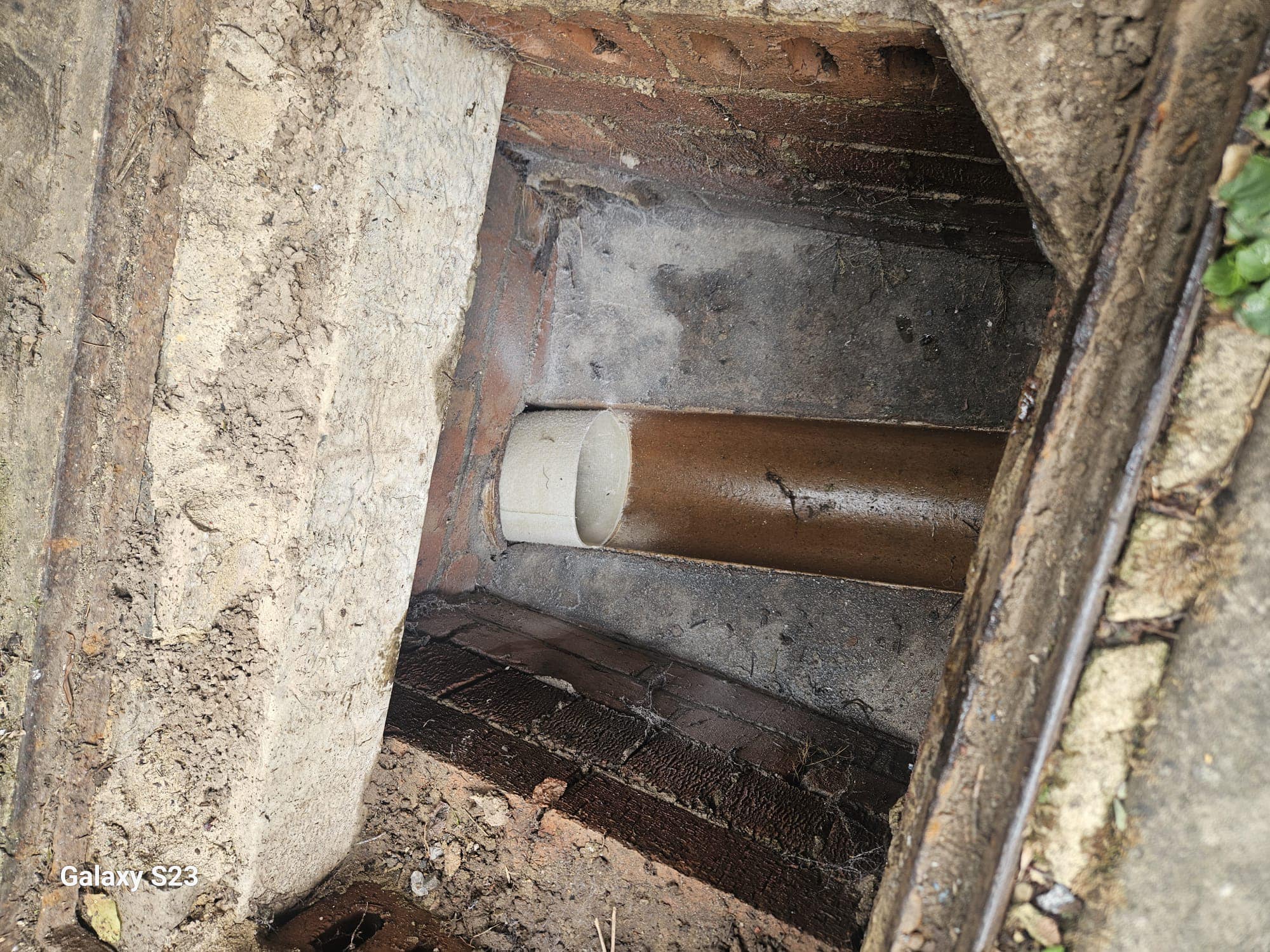 An open drain inspection chamber showing drainage pipes, likely undergoing inspection or repair.