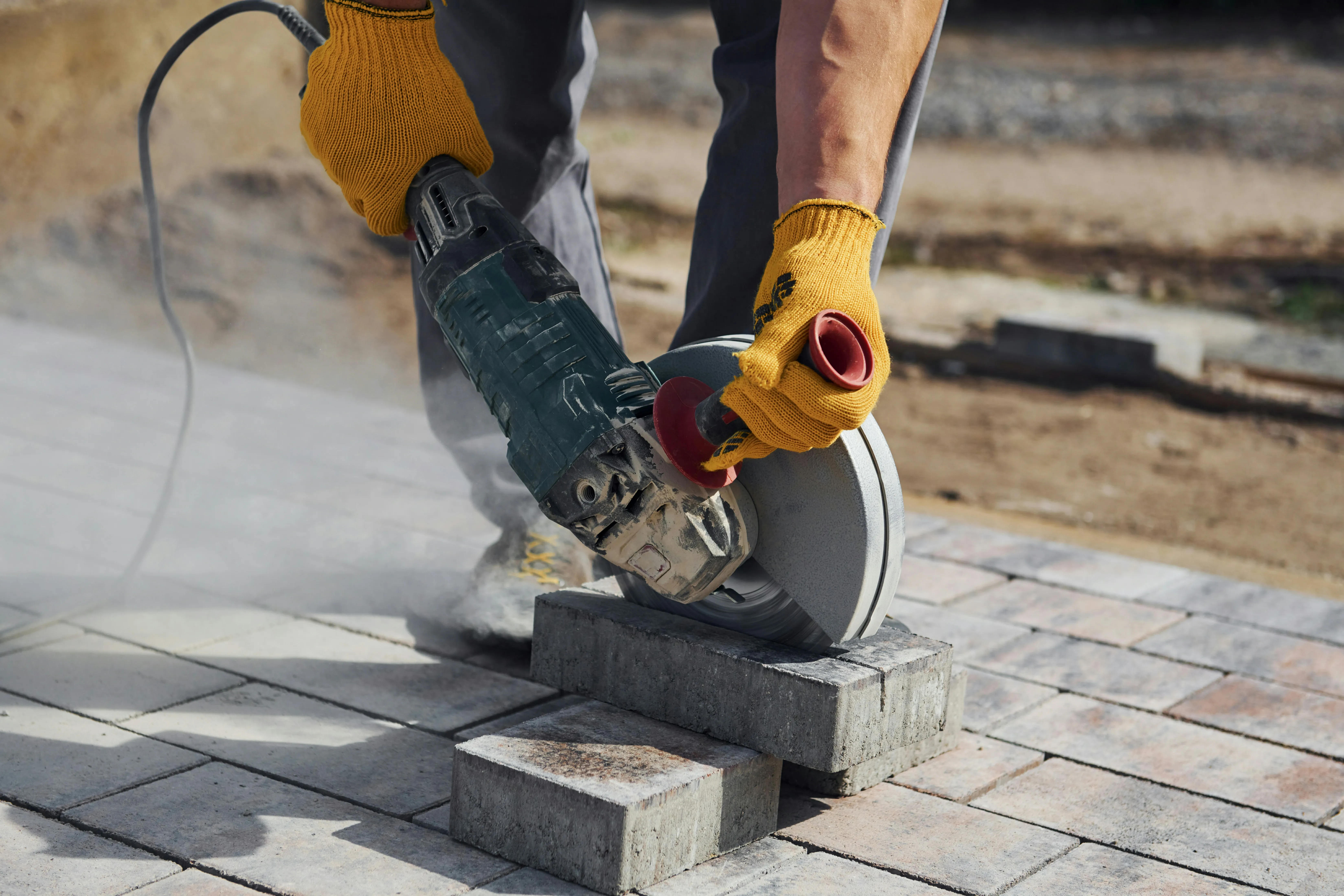 A builder cutting a block paving stone with an angle grinder for a driveway or patio project.