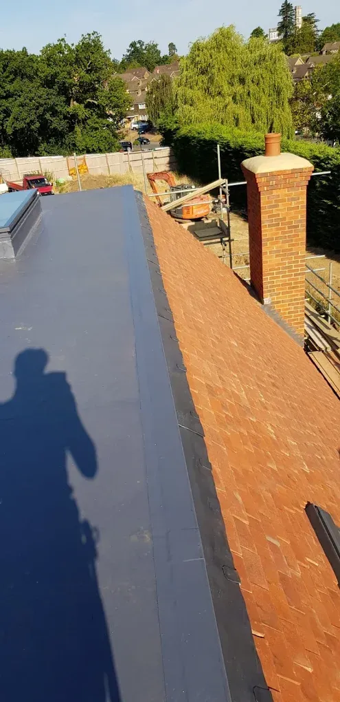 Residential roof replacement in progress with tiled and flat sections, chimney, and scaffolding.