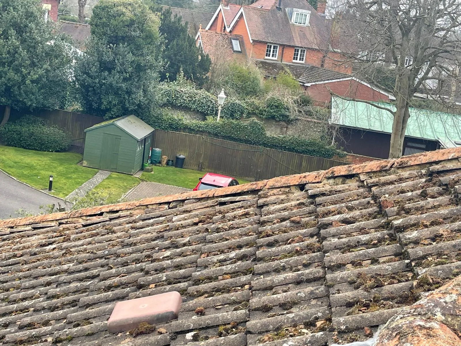 A close-up view of an aged, moss-covered tiled roof on a residential property, highlighting the need for roof cleaning services.