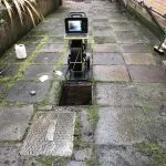 CCTV drain survey equipment with a camera being lowered into an open manhole or drain access.