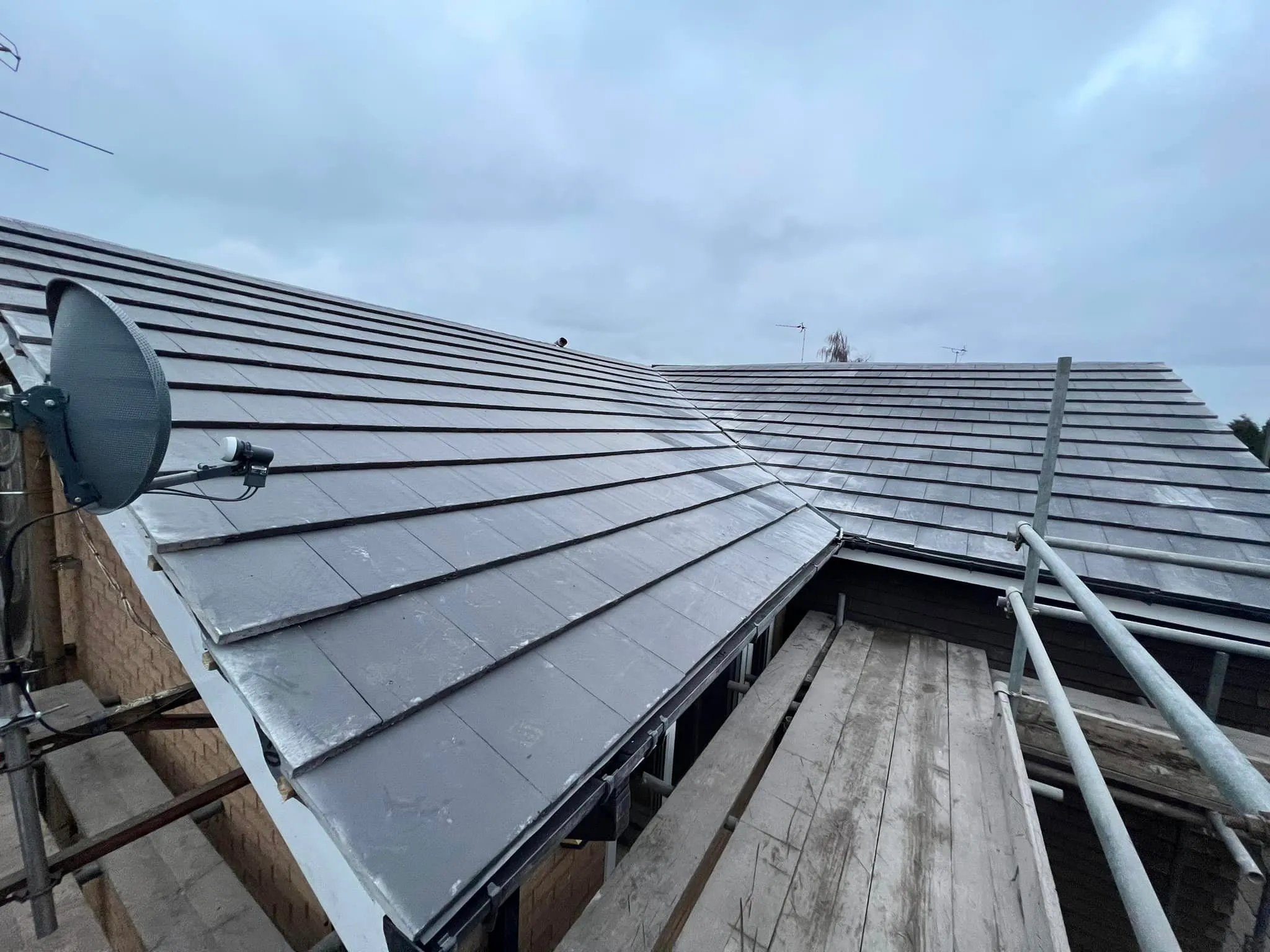 Pitched roof with dark tiles, scaffolding, and satellite dish during roofing work