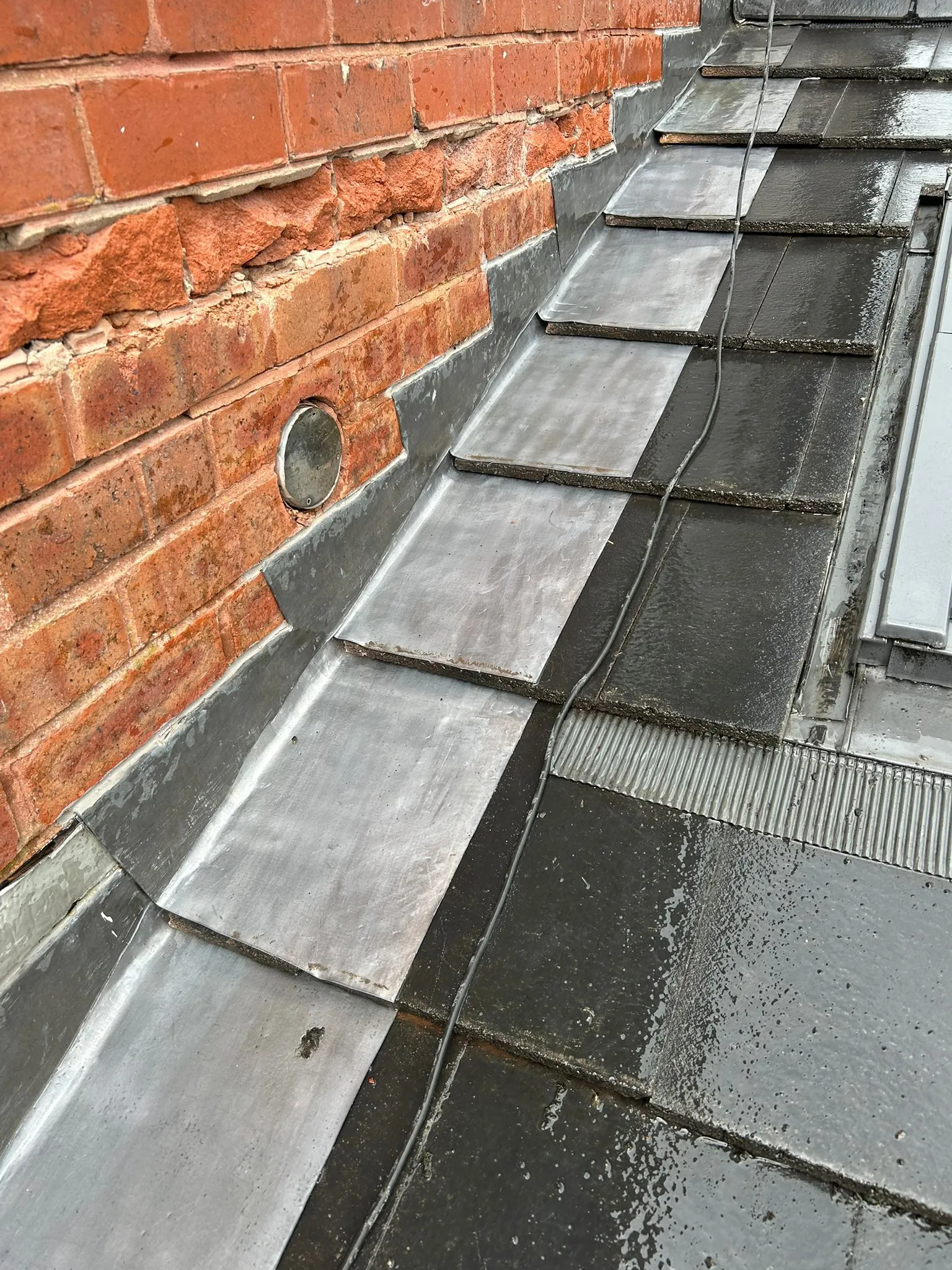 Lead flashing and roof tiles meeting a red brick wall with minor brickwork damage.