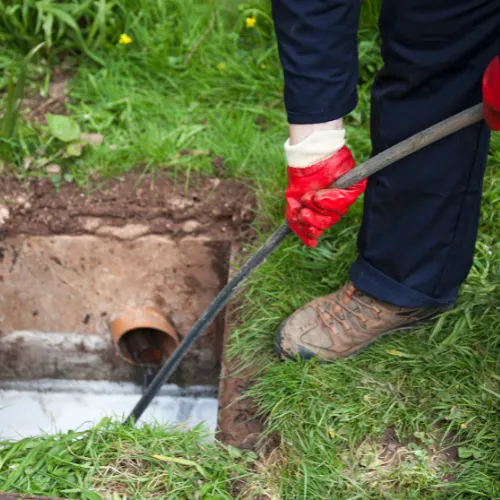Technician using a drain rod to clear a blocked outdoor drain