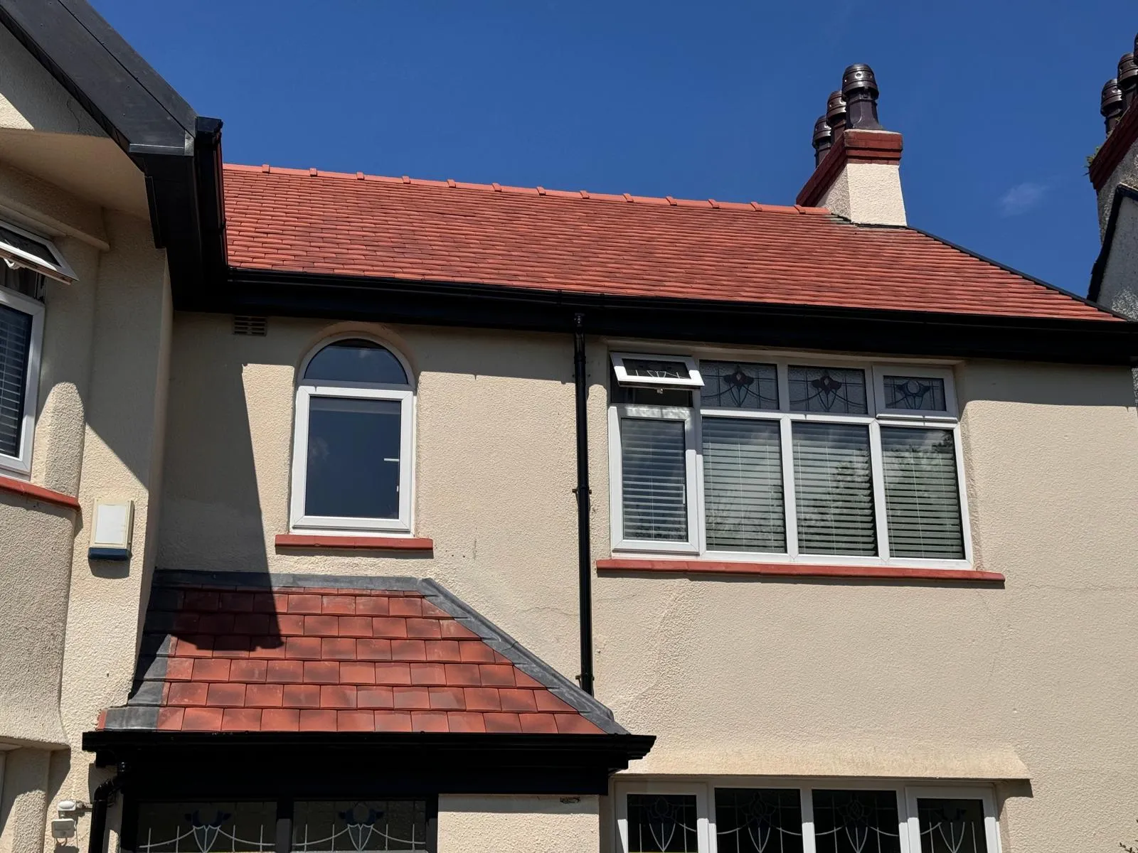 A house with a newly fitted red tiled roof, black gutters, and cream walls on a sunny day.