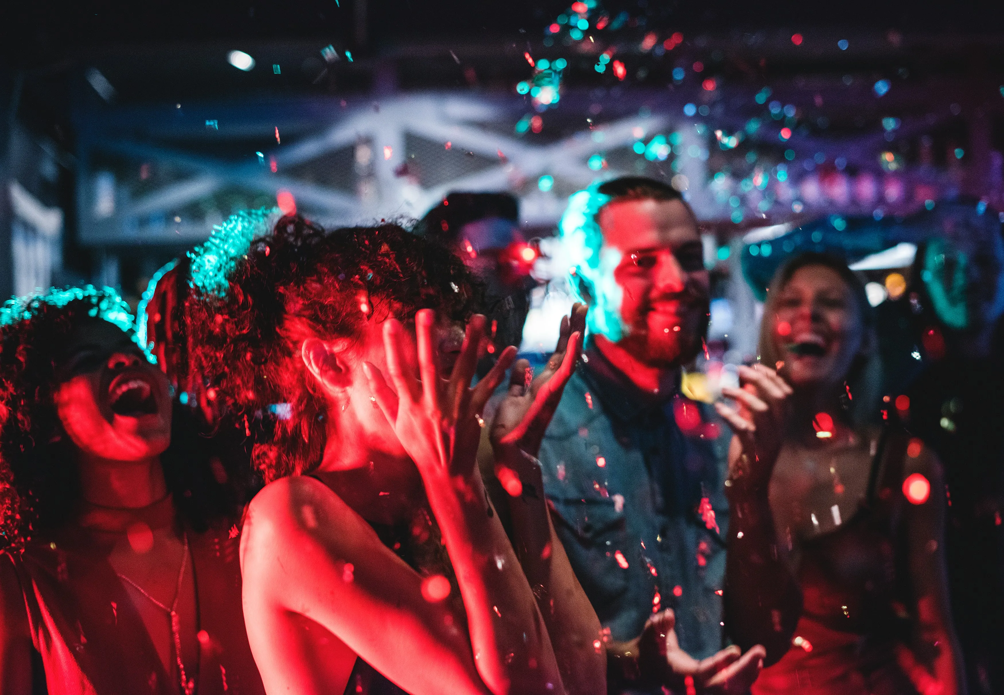 A group of happy party-goers dancing and laughing under colourful disco lights with confetti, showcasing lively entertainment.