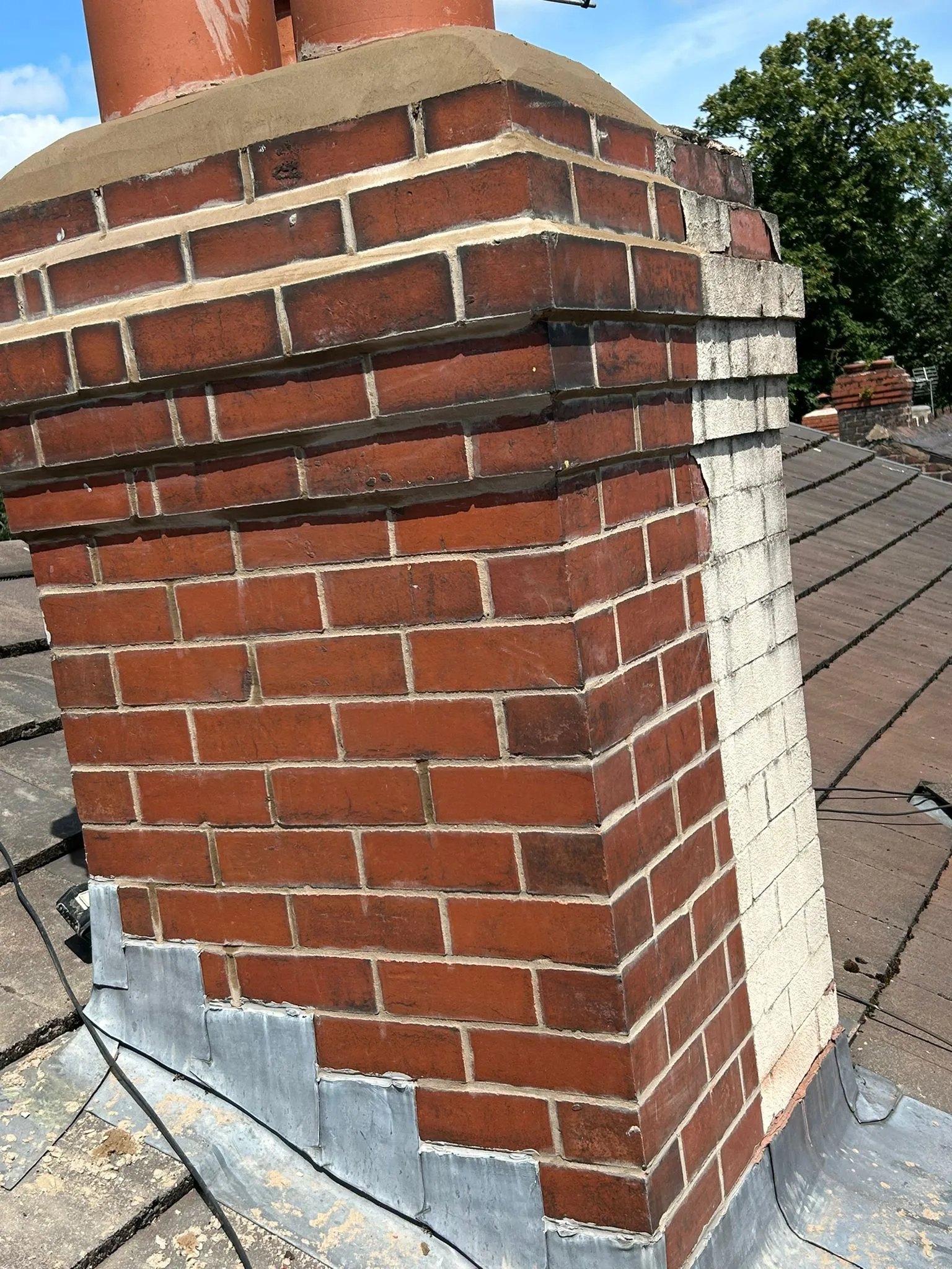 A brick chimney stack on a roof with lead flashing, showing both old red brick and new white repointing.