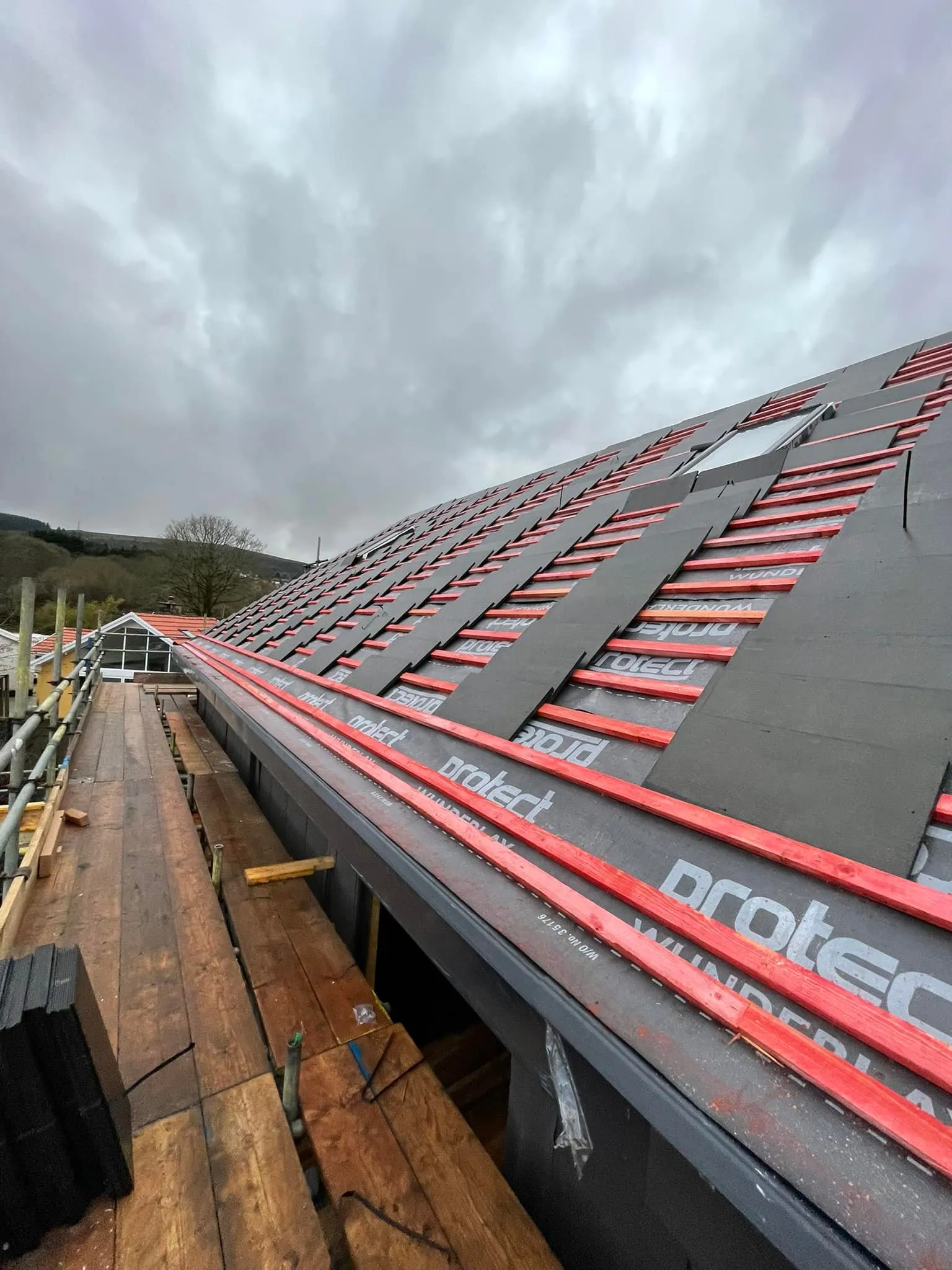 Pitched roof under construction with grey membrane, red battens, and scaffolding.
