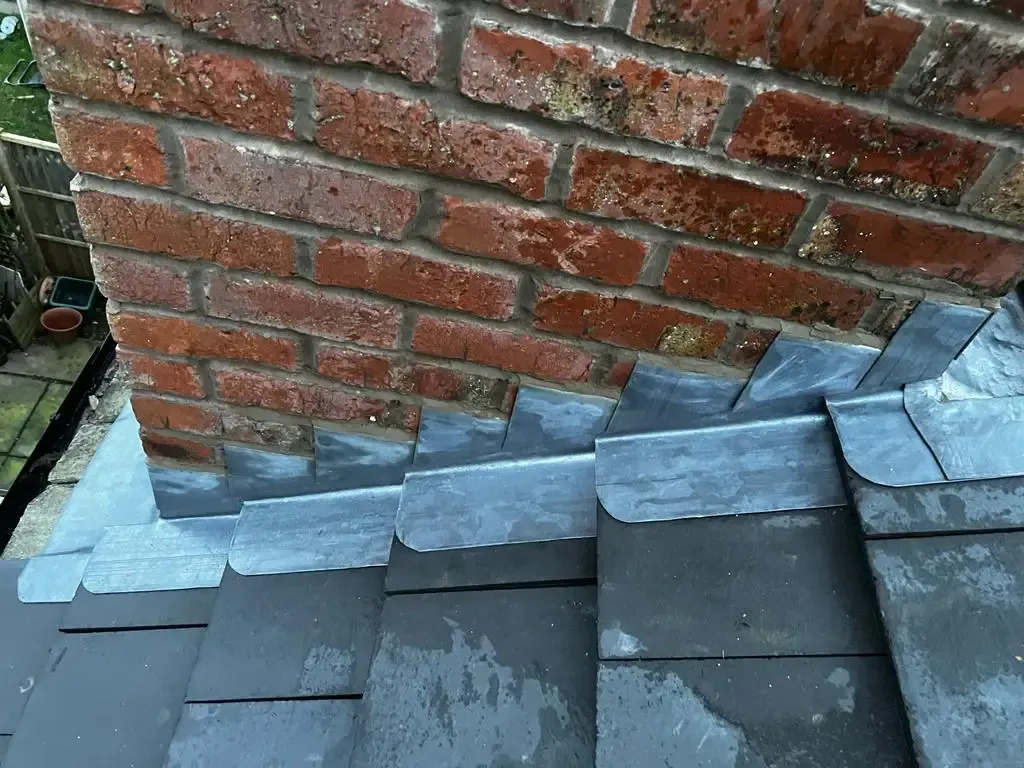 Lead flashing detail at the base of a brick chimney on a tiled roof.