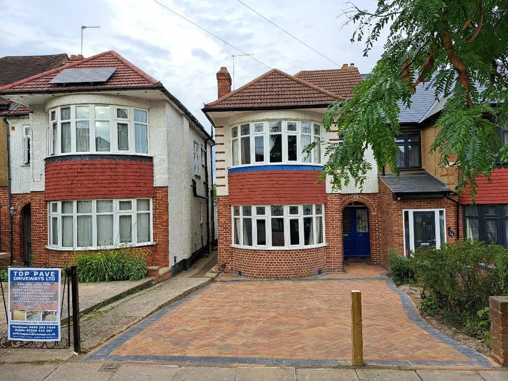 A modern block paving driveway featuring red and grey blocks in front of a traditional red brick and white house, with a Top Pave Driveways LTD advertising board.
