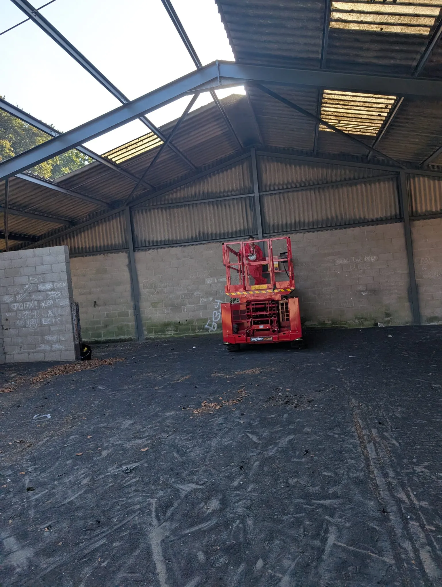 An asbestos removal operative in a red scissor lift working on a corrugated industrial roof.