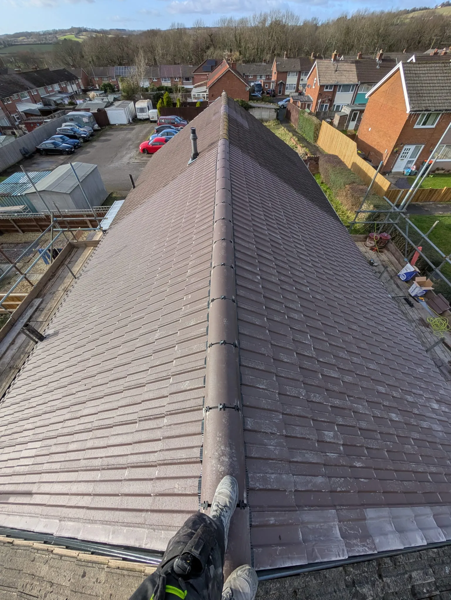 High-angle view of a new brown tiled pitched roof on a residential property, overlooking a neighborhood and distant hills.