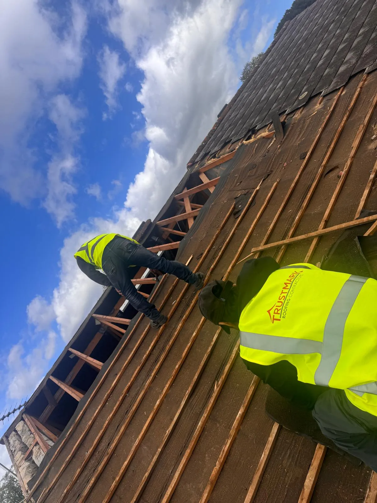Two Trustmark Roofing contractors on a pitched roof, installing wooden battens and a new roofing underlay.