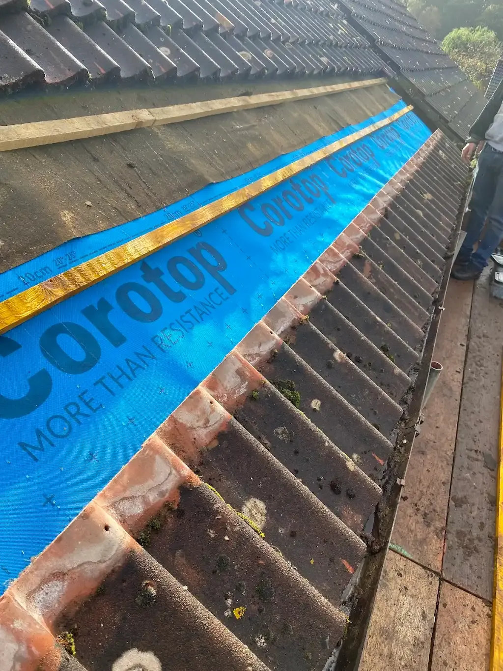 Roof tiling in progress: Installing concrete or clay tiles over timber battens and blue Corotop underlay on a pitched roof.