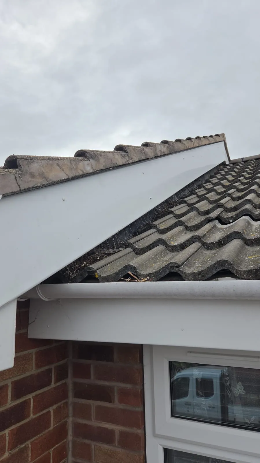 Residential roofline in Leicestershire with grey concrete tiles, white UPVC fascia, guttering with minor debris, and bird prevention spikes.