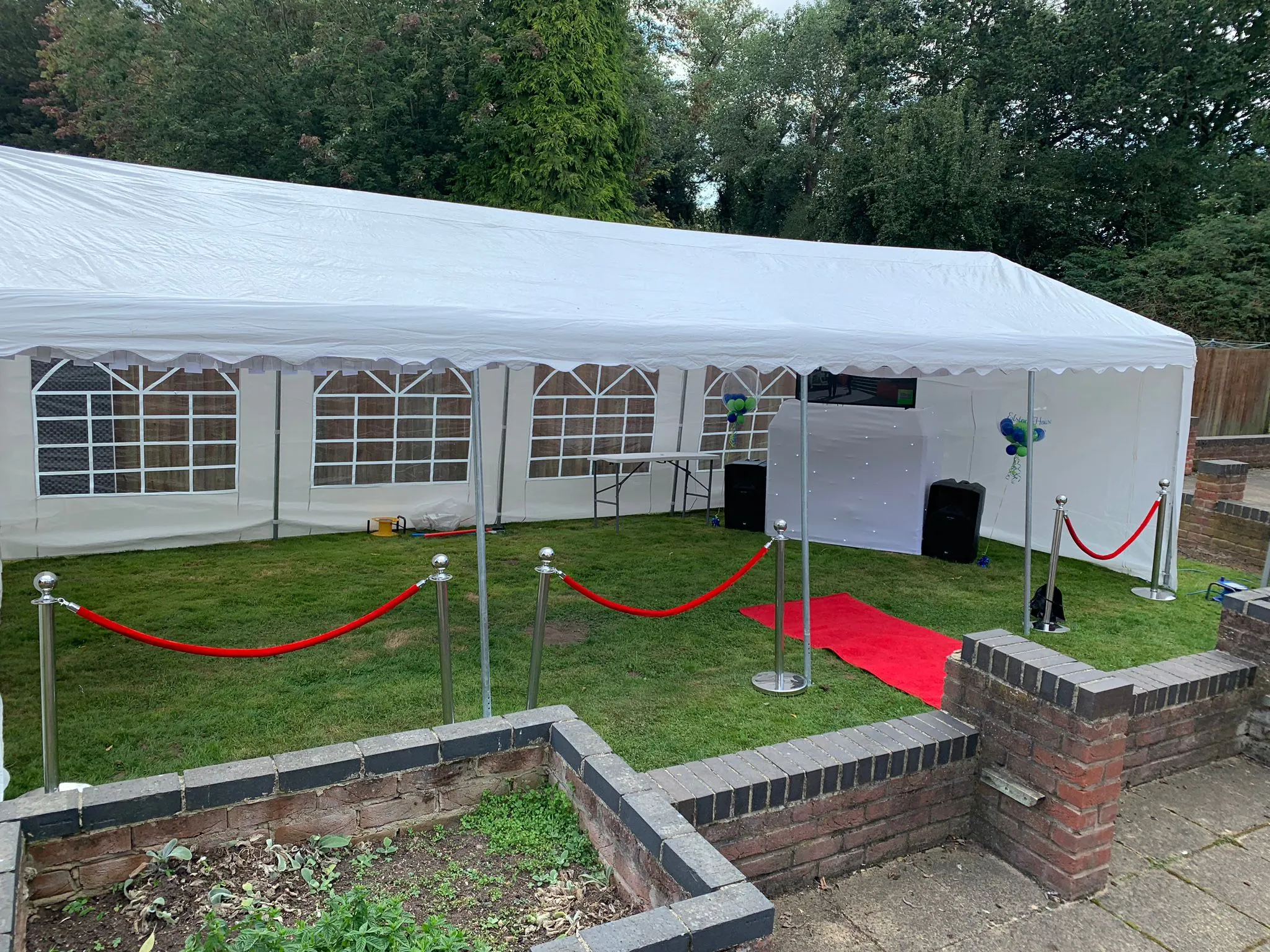 White marquee setup for an outdoor party with red carpet, VIP ropes, and a professional DJ station visible inside.