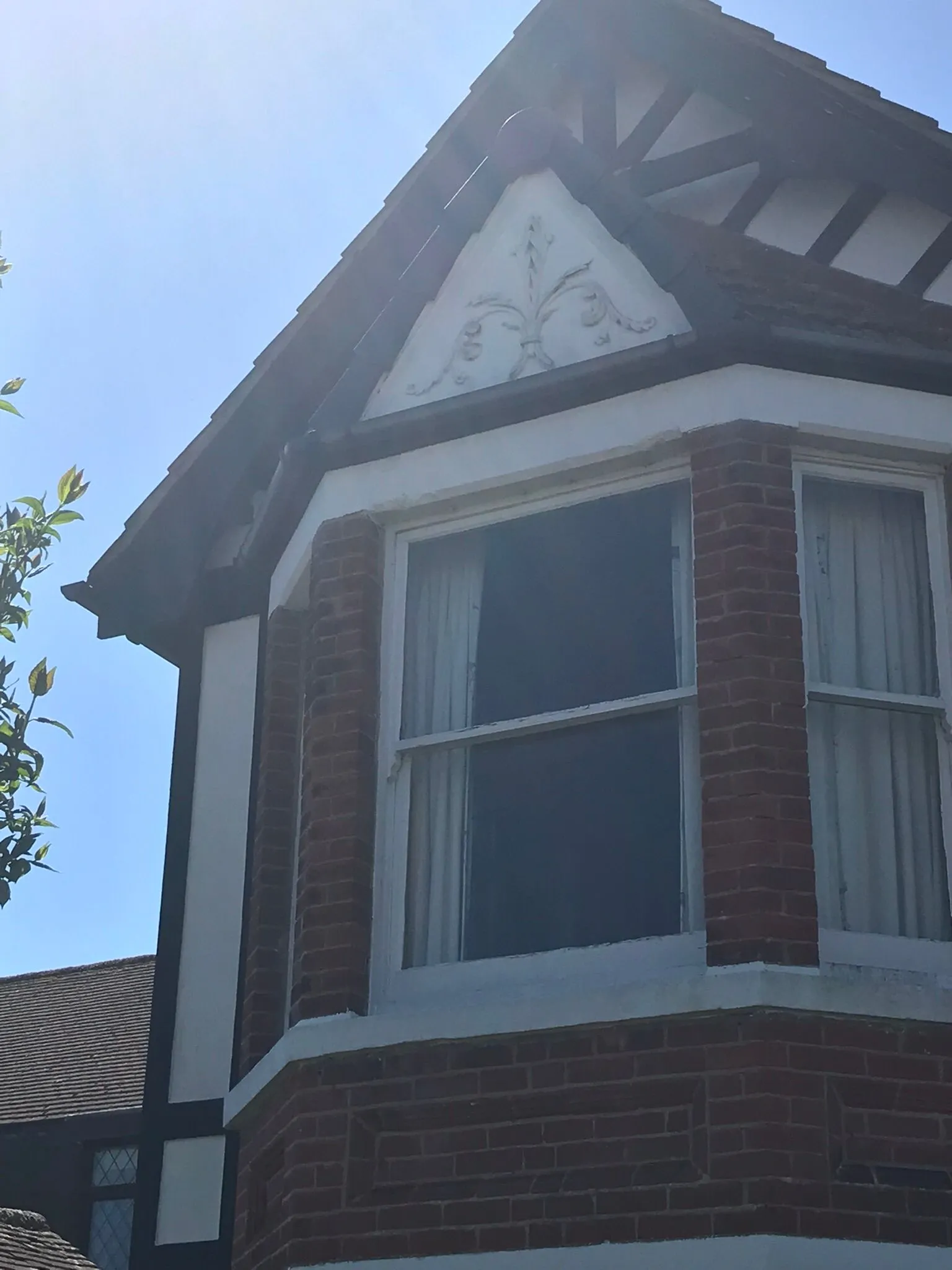 A close-up of the upper facade of a house with a bay window, a pitched tiled roof, and decorative white gable elements.