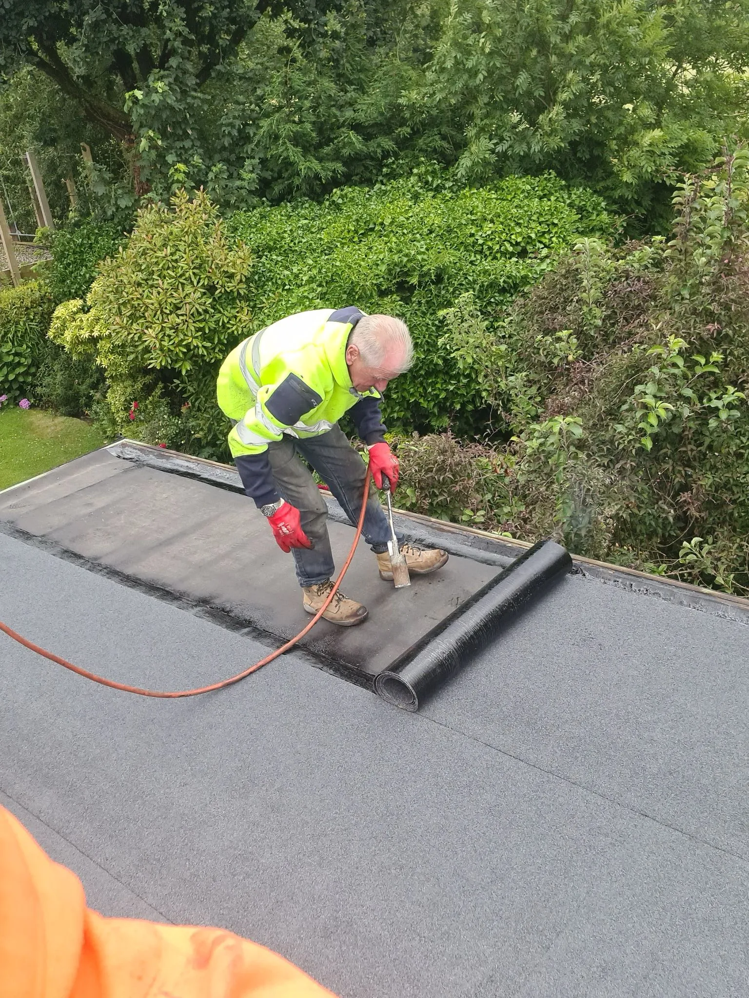 An M. Woodward Roofing expert installing torch-on felt flat roofing on a residential property, ensuring a durable and waterproof seal.