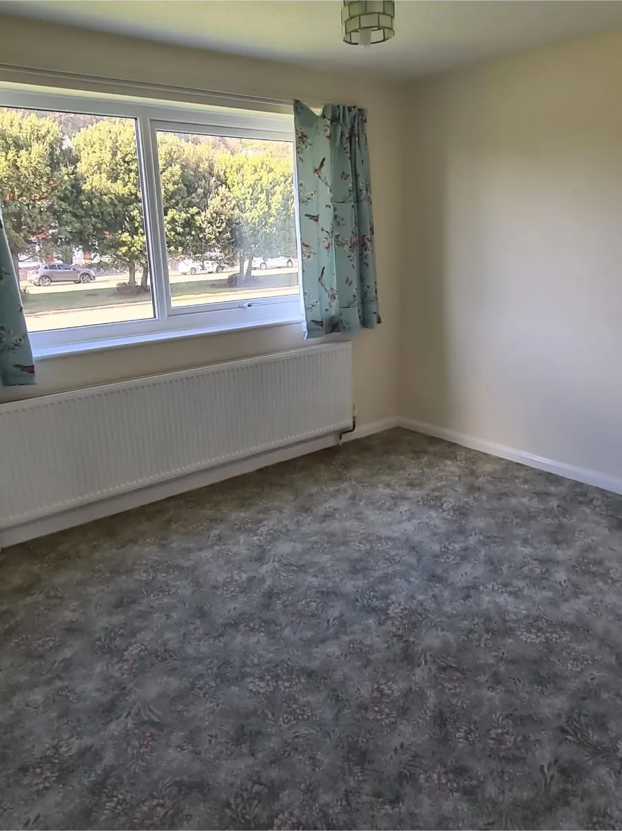 An empty room with a window, radiator, and patterned carpet, showcasing a property after a professional house clearance service.