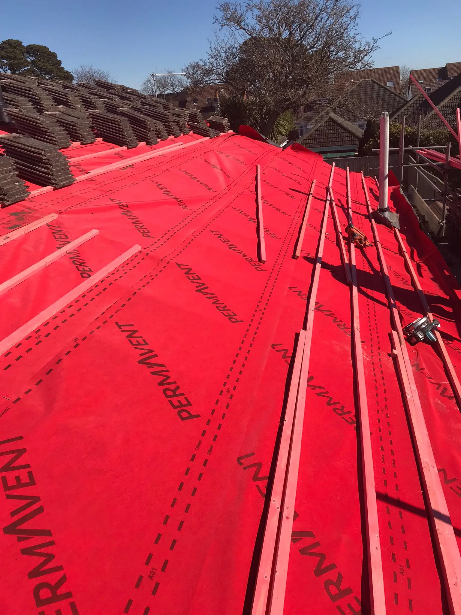 New pitched roof construction with red underlayment, timber battens, and neatly stacked dark roof tiles in Southampton.