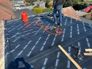 Roofer installing a new black flat roof membrane with a gas torch and tools