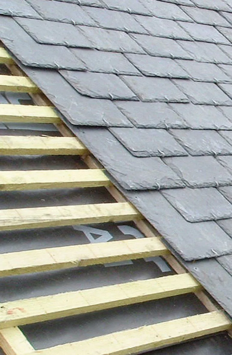 Close-up of new slate roof installation in progress, showing tiles over battens and felt.