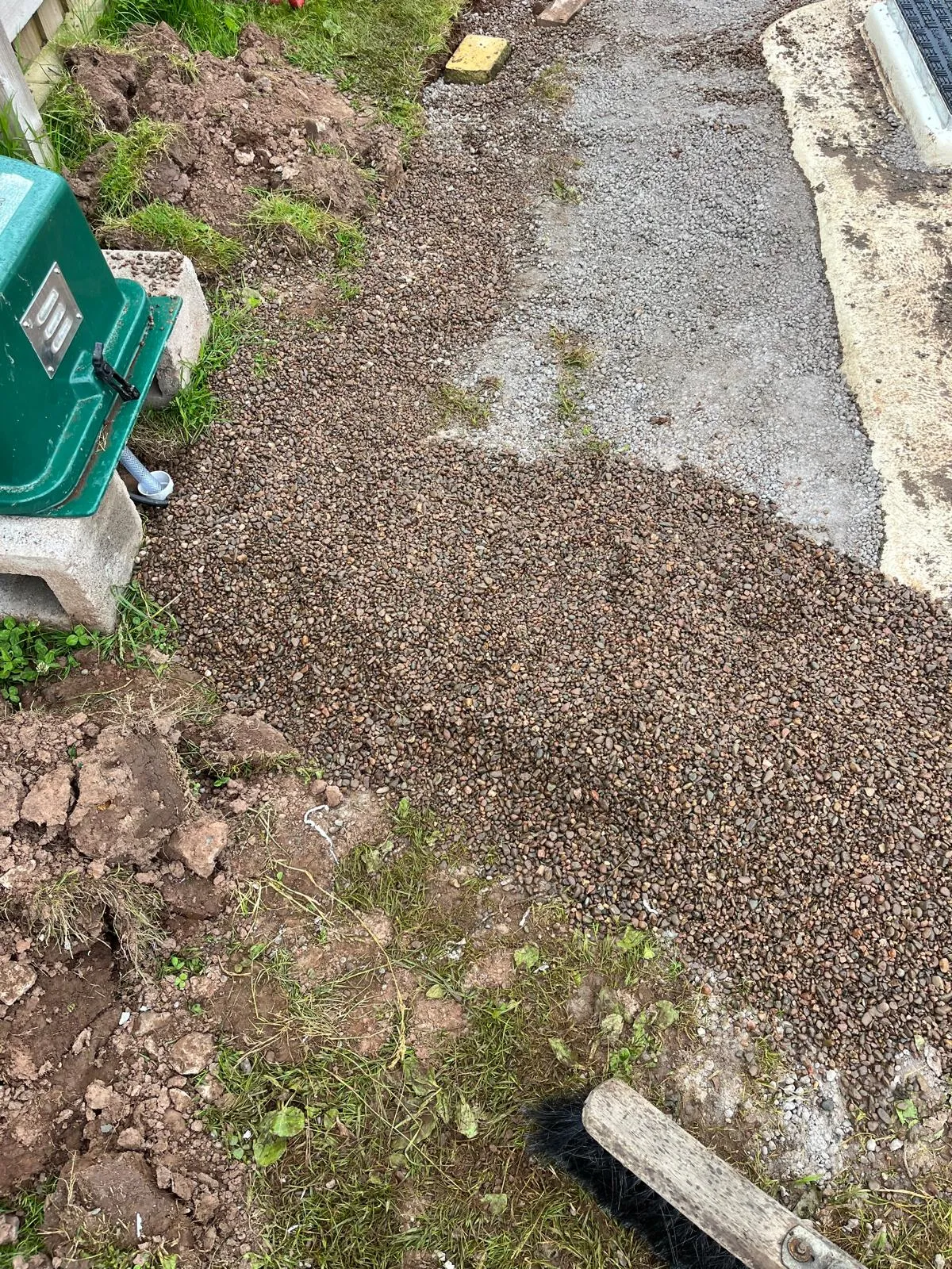 A green pump station being installed or maintained, with surrounding gravel and excavated earth.