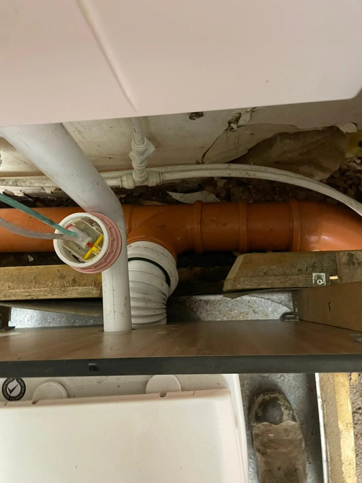 Under-sink plumbing with orange drain pipes, white water pipes, and electrical wiring connections.