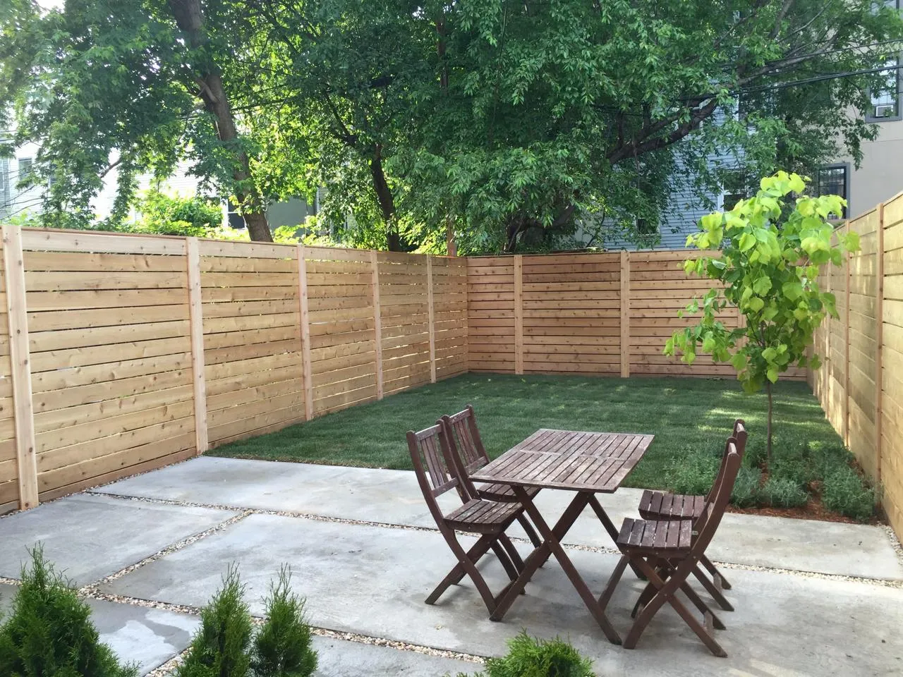 Modern landscaped garden with new wooden fence, concrete patio, and lawn.