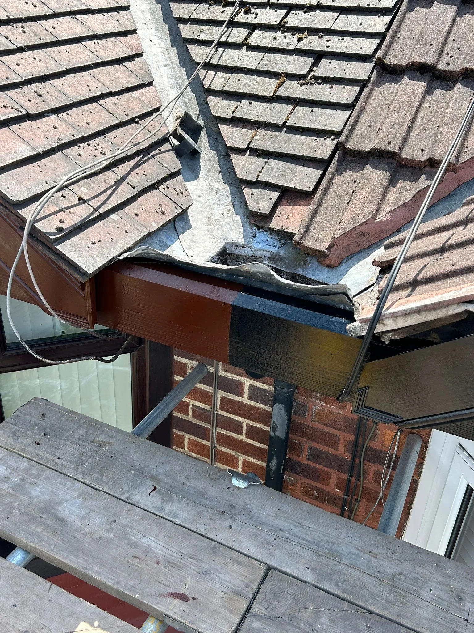 Residential roof showing repair work on the fascia board and guttering at a roof valley, with scaffolding present.