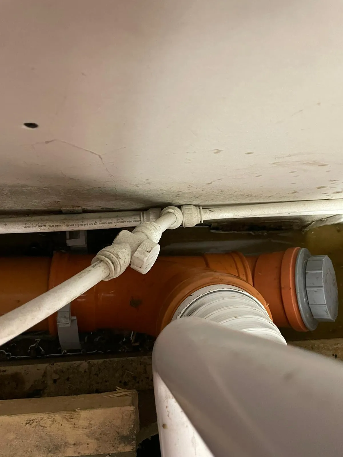 Close-up of orange drainage pipes and white water supply lines in a crawl space, highlighting plumbing repairs or installations.