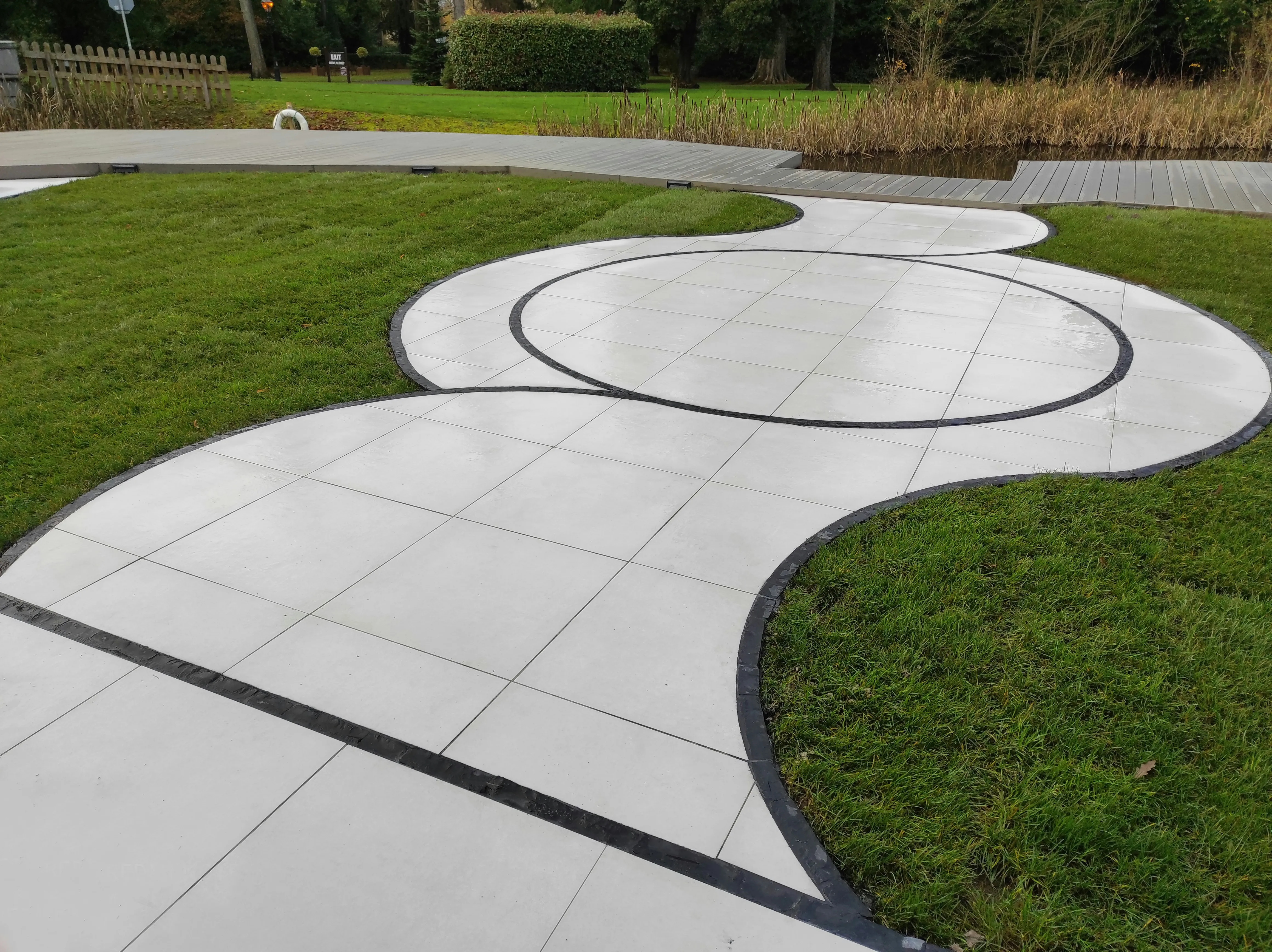Modern curved garden patio with light grey paving slabs and dark border
