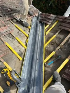 Roofers installing lead flashing in a roof valley during a new roof construction or major repair, with tools visible.