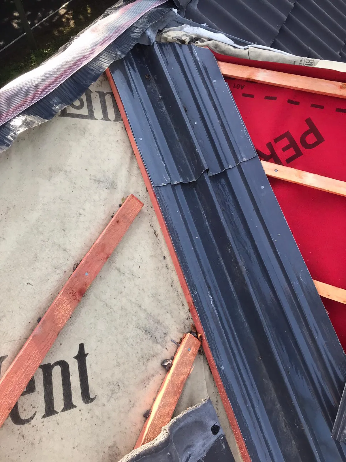 Roofing in progress with dark corrugated panels, red and grey underlayment, and timber battens.