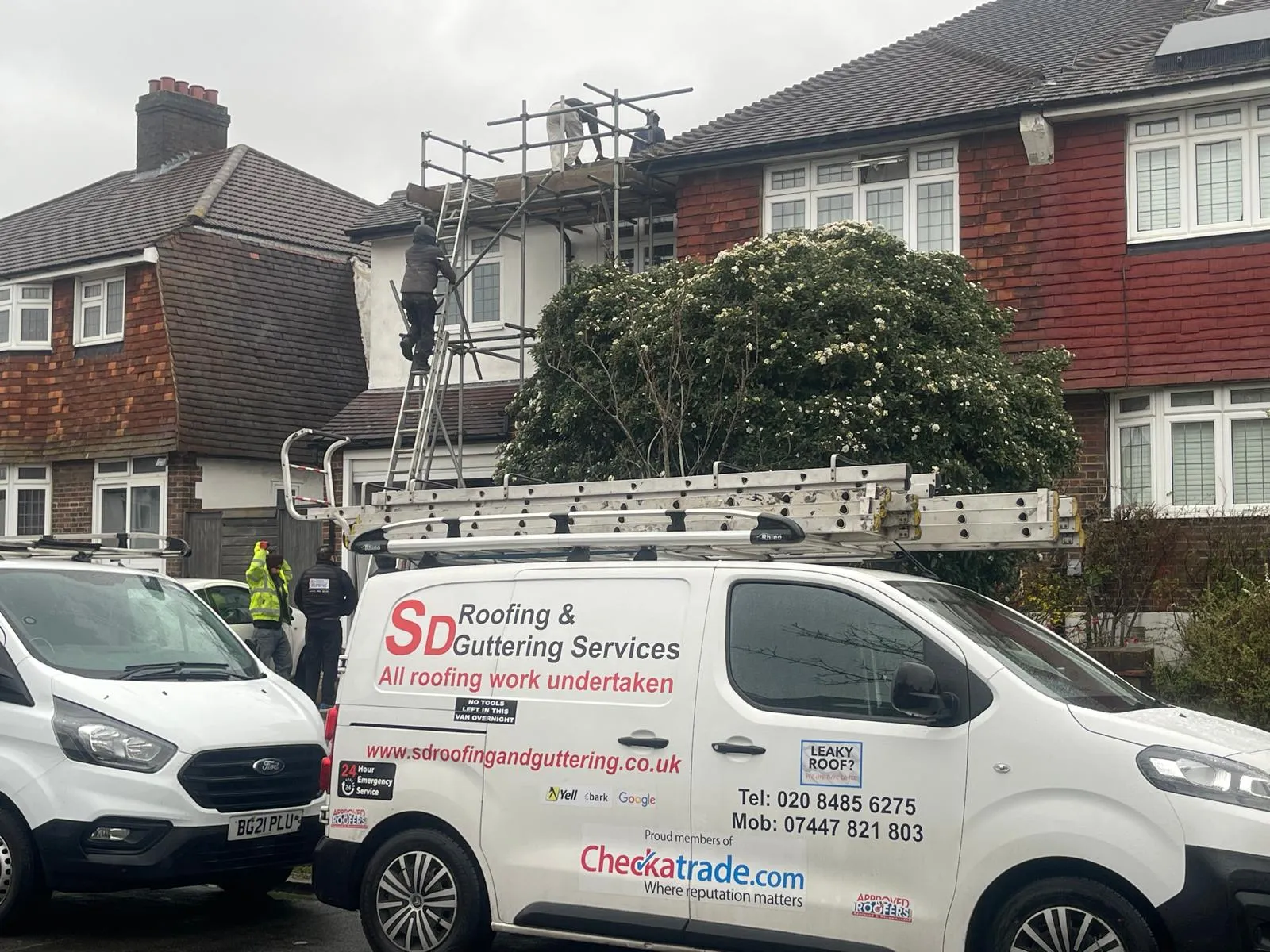 SD Roofing And Guttering branded van parked outside a house with scaffolding where roofers are performing roof work.
