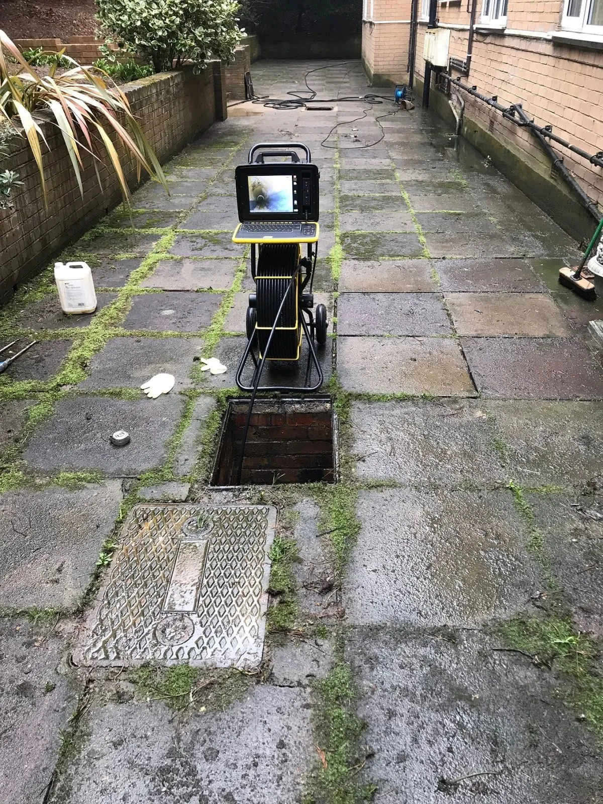CCTV drain survey in progress on a residential property, with camera equipment and an open manhole.