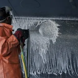 Drainage technician performing high-pressure drain jetting or descaling, wearing protective gear.