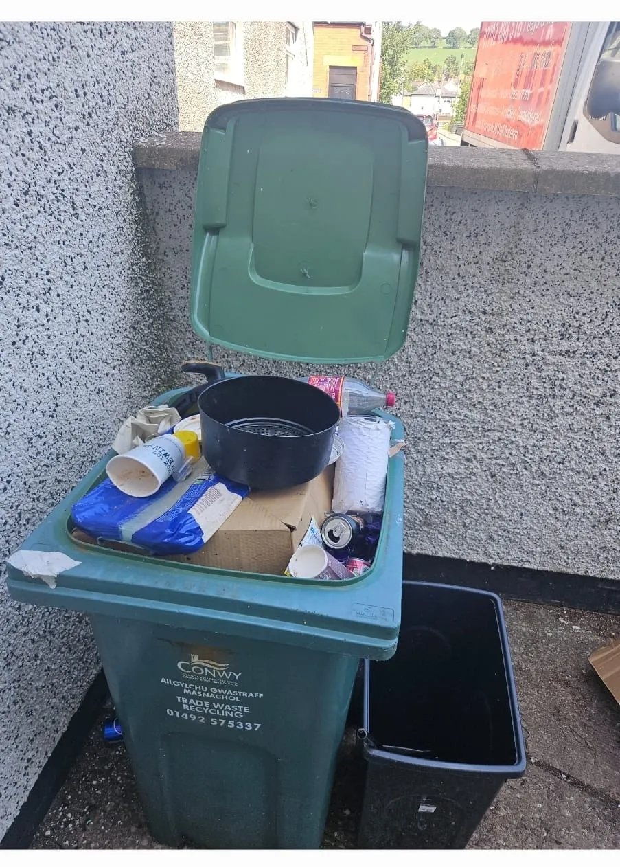 Overflowing green wheelie bin full of mixed household rubbish, highlighting a need for rubbish removal and waste clearance services in the Conwy area.